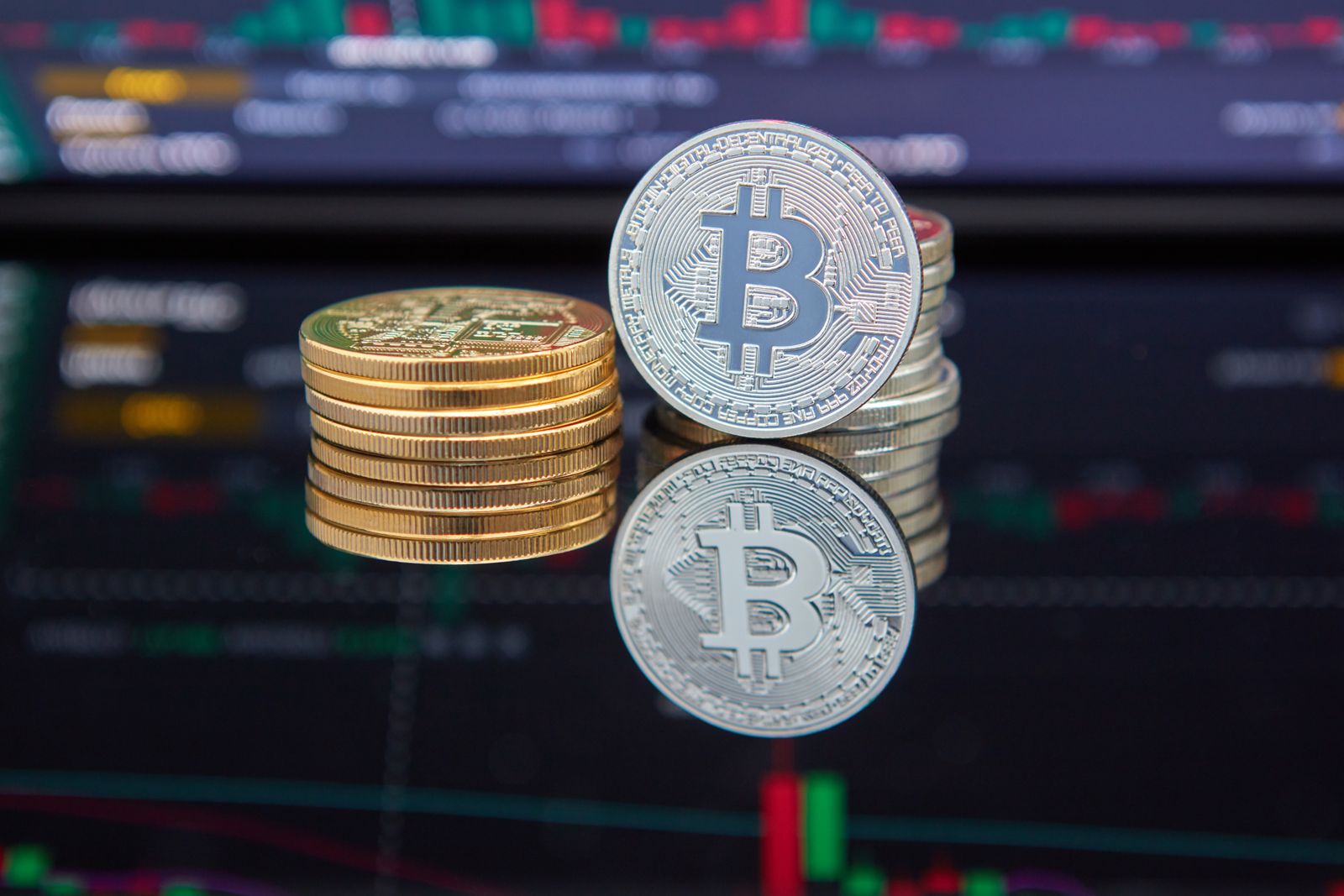Koin Bitcoin bertumpuk di depan layar grafik perdagangan kripto